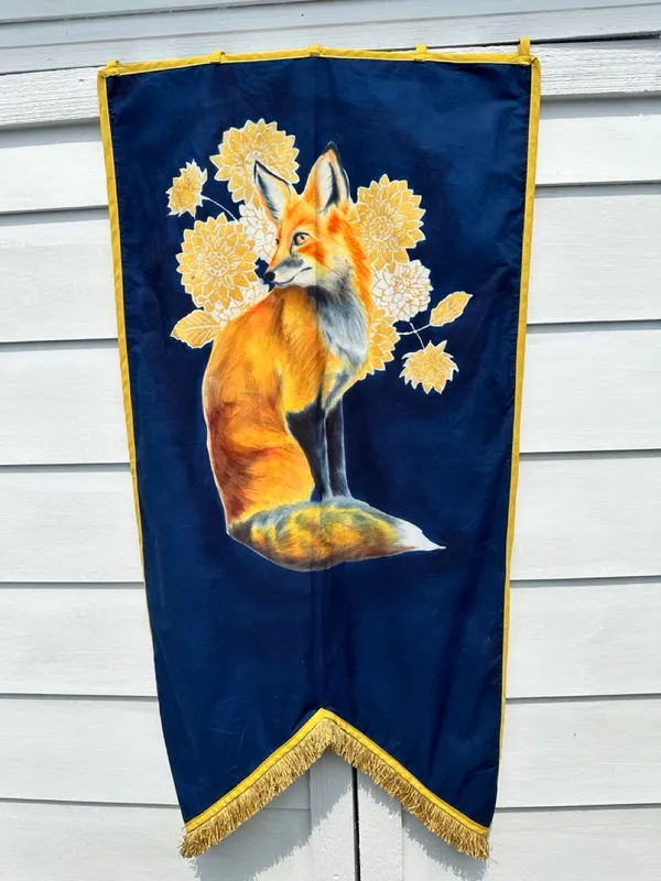 red fox sitting and looking over shoulder, on a field of gold and white flowers on a navy banner