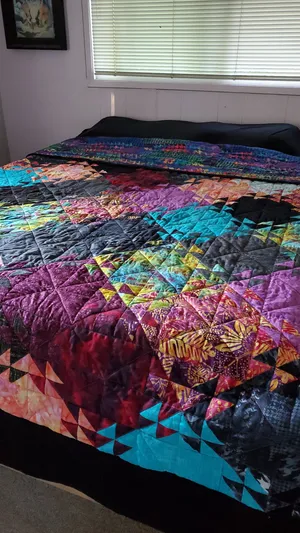 Large quilt made with black and brightly colored squares that shatter into triangles to look like ripples in water