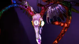 A winged deer skull that resembles a sugar skull, lit up with rainbow colors from within