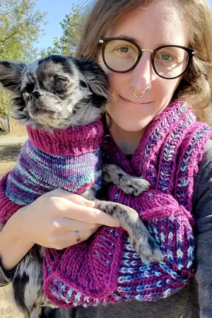 Stephanie wearing a purple and blue brioche cowl, holding her chihuahua in a matching sweater