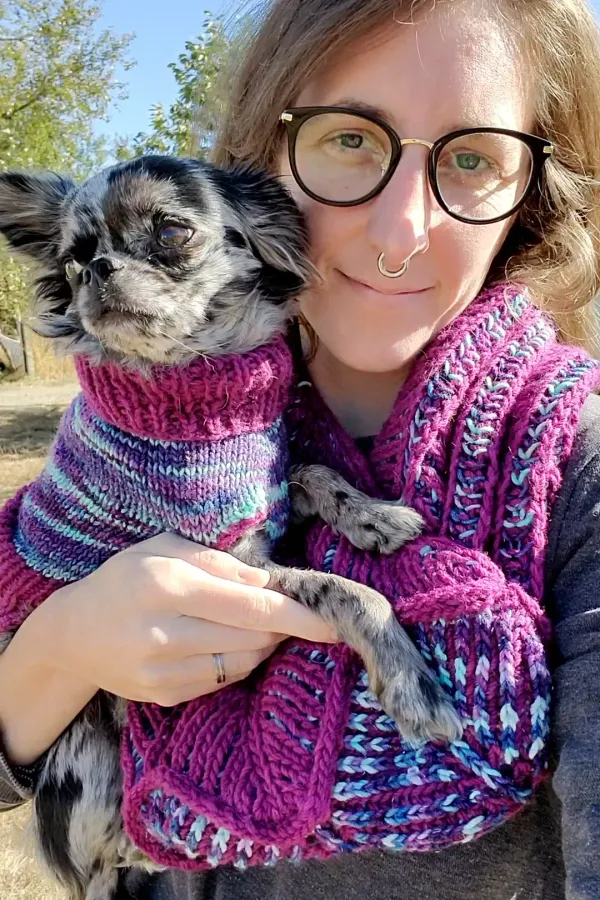 Stephanie wearing a purple and blue brioche cowl, holding her chihuahua in a matching sweater